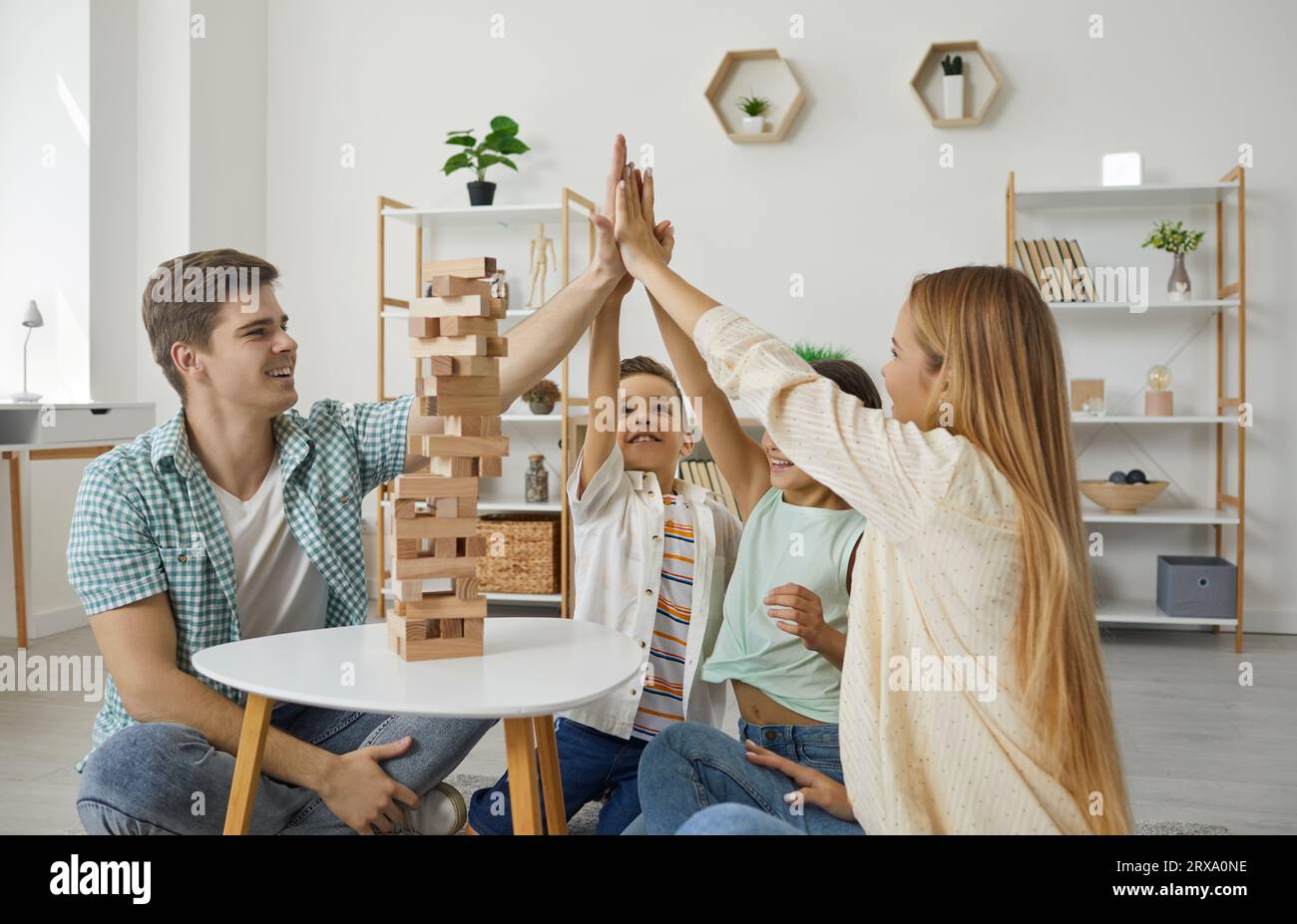 Happy family with two children are playing tumbling tower giving high five sitting on floor at home. Stock Photo