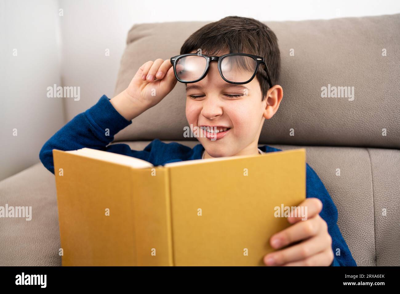 Child suffering eyes strain trying to read a book at living room Stock