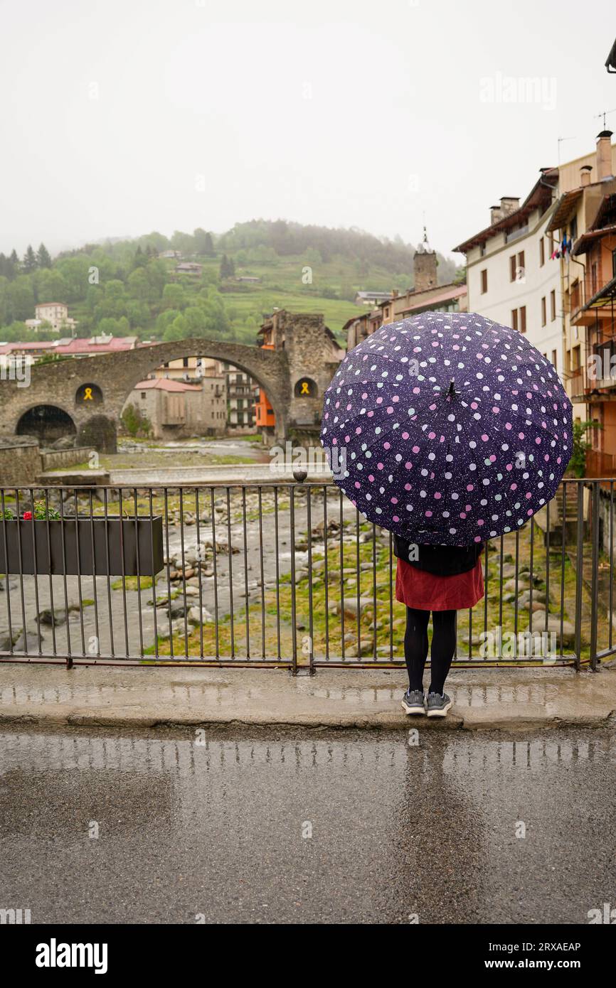 woman tourist protecting herself from the rain with an umbrella in wintertime in Camprodon. Bad weather. Rear view Stock Photo