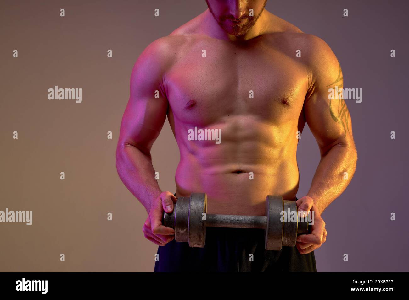 close up cropped shot of male's body with perfect six-packs, abs with dumbbell, tired sportsman takes break,isolated brown background Stock Photo