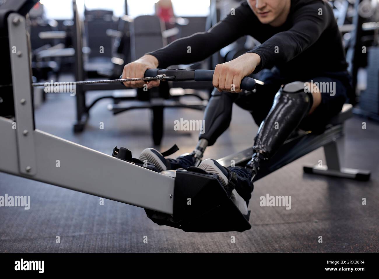 disabled person uses a rowing machine at sport center, cropped shot, focus on artificial legs lifestyle health and body care Stock Photo