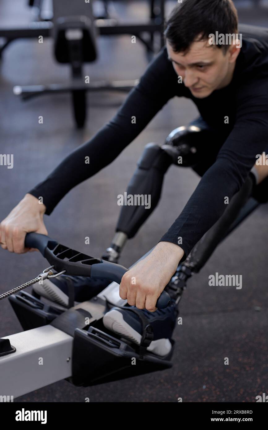 motivated sportsman with artificial legs limb working out in gym on rowing machine, lifestyle spare time, health and body care, cropped photo. focus o Stock Photo