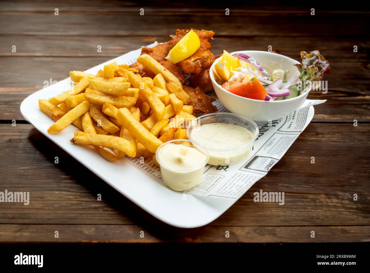Fried fish, french fries, salad and sauces served on a white plate with newspaper decoration Stock Photo
