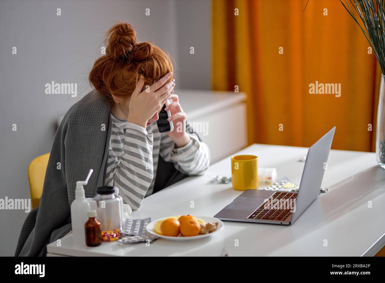 exhausted unhappy girl covered with plaid sitting on chair with hand, palm on her face, working on PC, talking on phone. Illness, work concept, busine Stock Photo