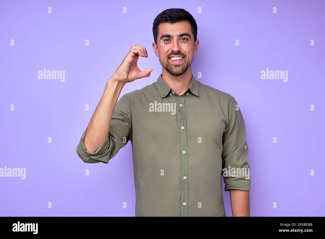 Young smiling deaf man wearing green shirt using sign language on blue background, male teaching deaf children to alphabet, education close up portrai Stock Photo