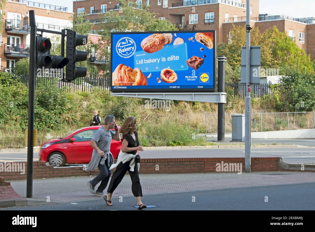 pedestrians cross the road in front of a digital billboard advertising the bakery of supermarket chain lidl with the phrase lidl bakery is elite Stock Photo
