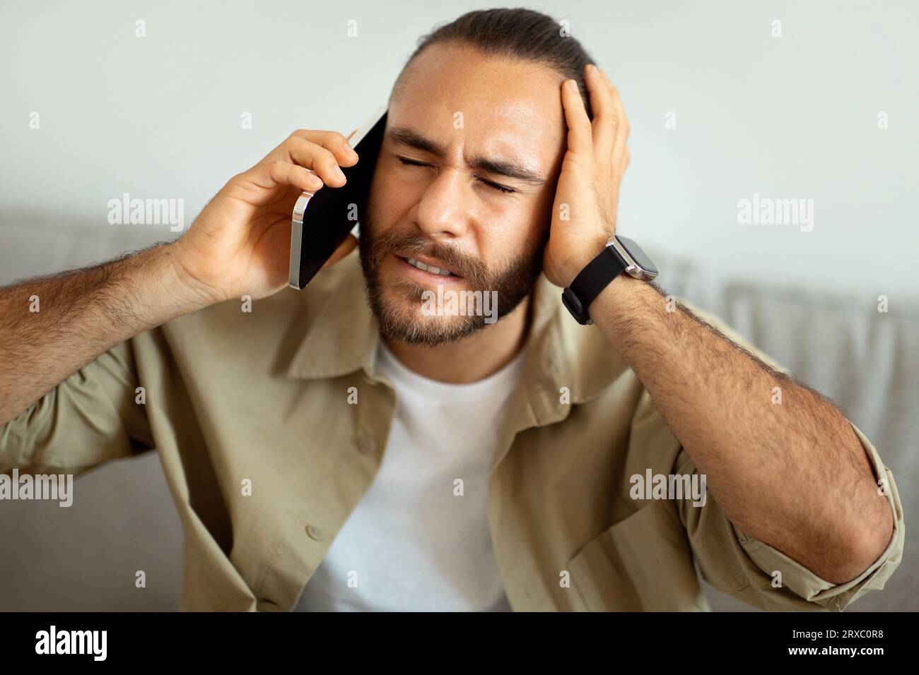 Stressed guy sitting on couch, having conversation on phone Stock Photo