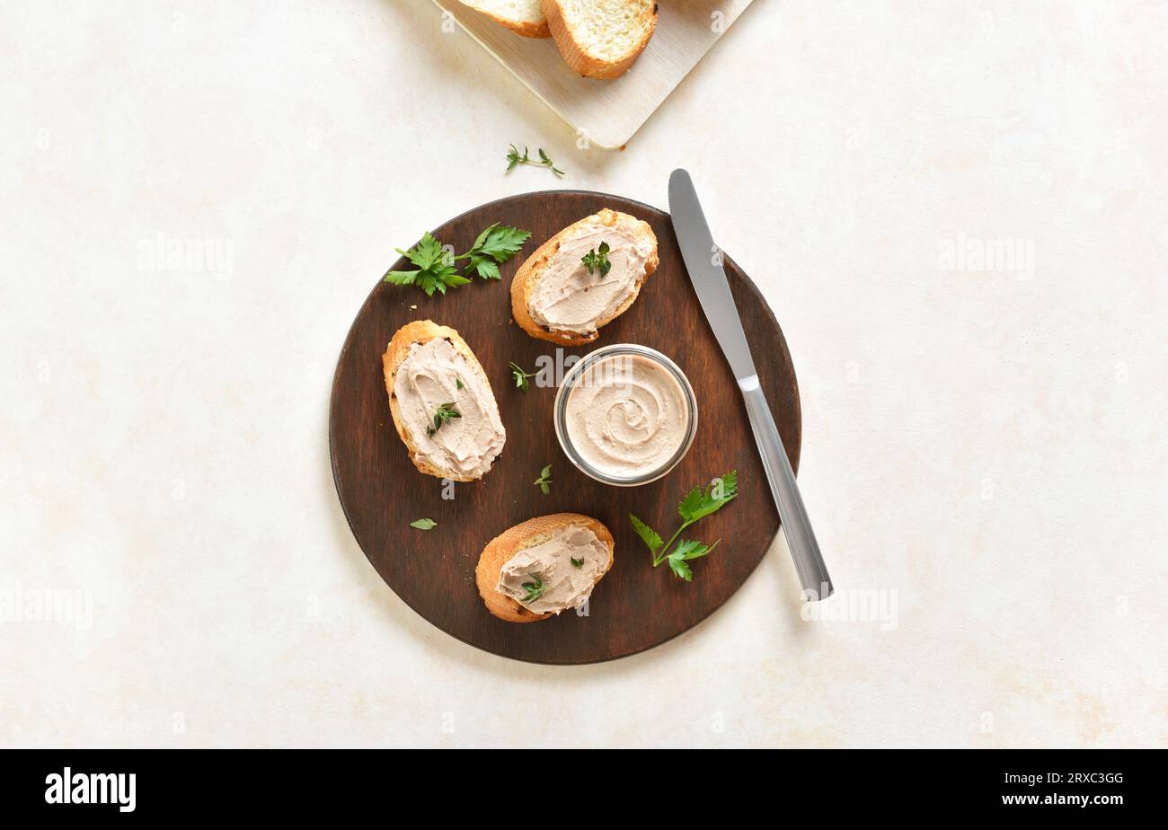 Chicken liver pate on toasted bread on wooden cutting board over light background with free space. Top view, flat lay Stock Photo