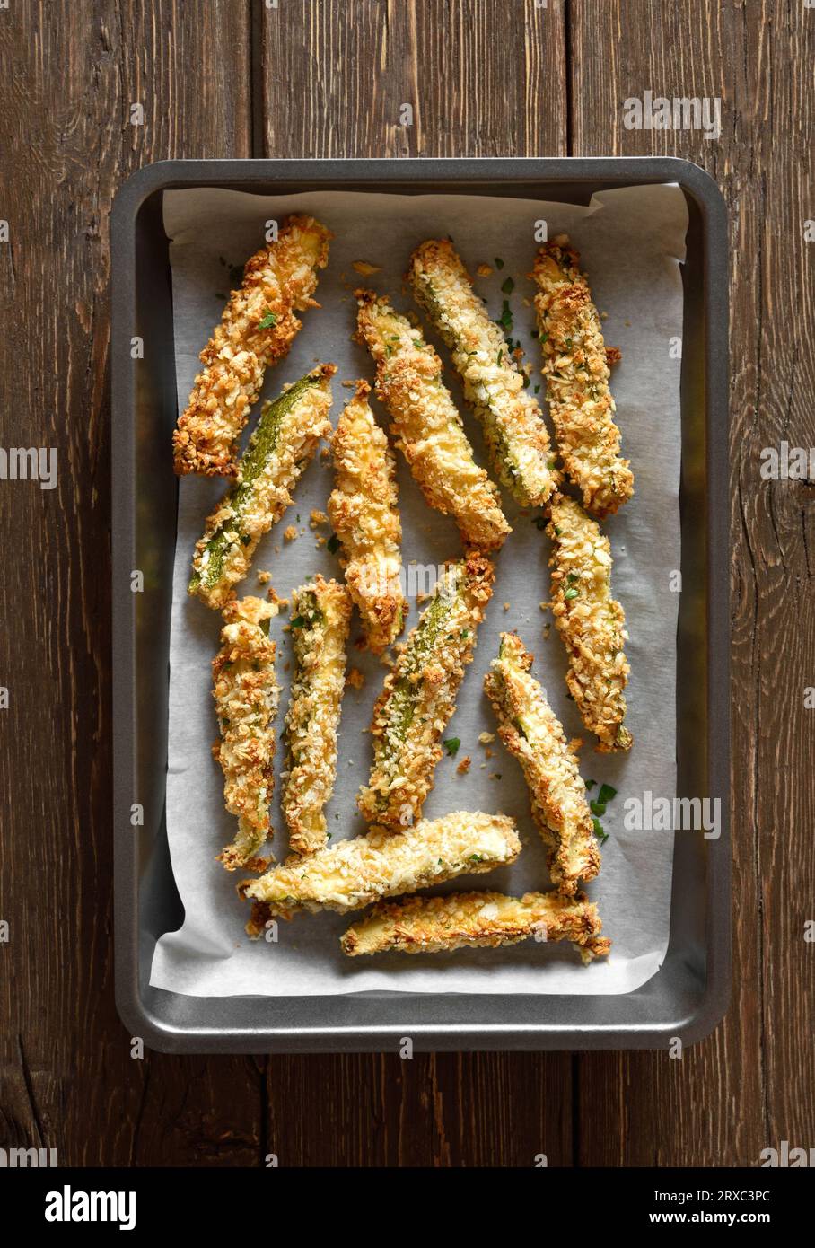 Zucchini sticks with panko breadcrumbs in baking dish over wooden background. Top view, flat lay Stock Photo