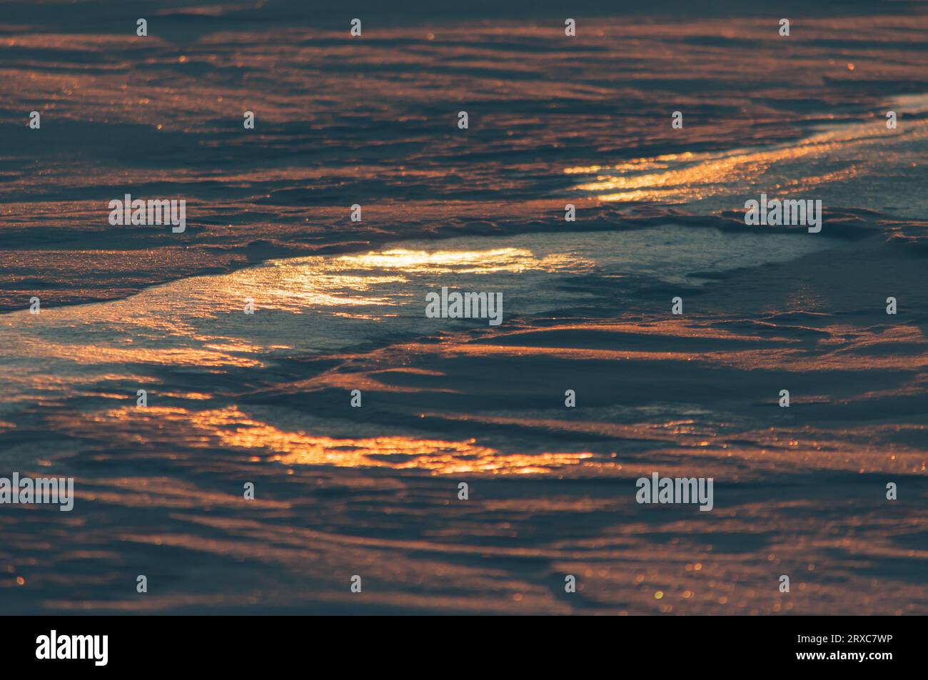 Patterns on frozen lake with setting sun coloring parts of the ice and snow Stock Photo