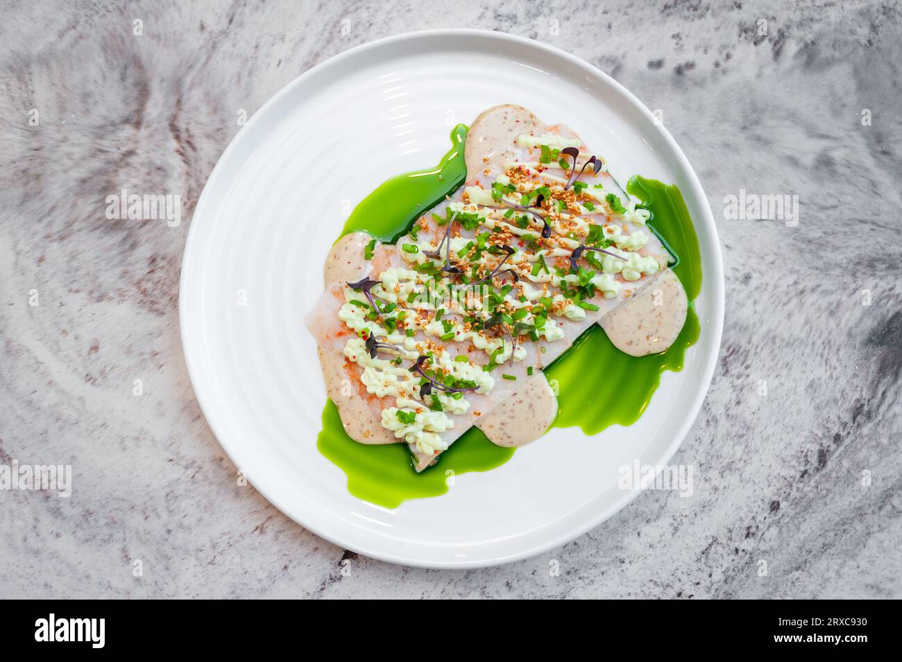 Shrimp tartare with sesame sauce and wasabi cream on a white plate on a marble table in a restaurant Stock Photo