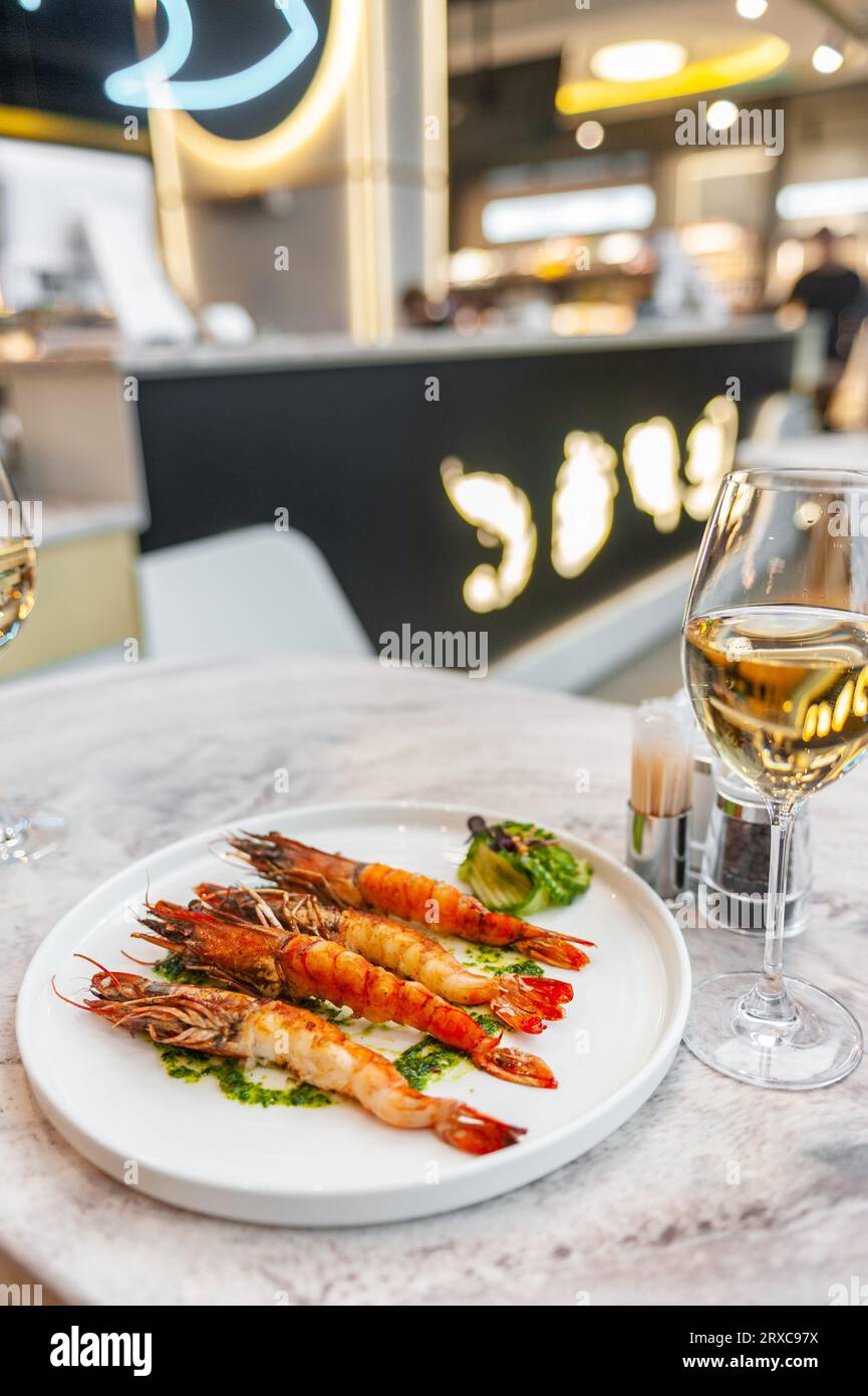 Langoustines with spinach sauce on a white plate on a marble table with a glass of white wine. High quality photo Stock Photo