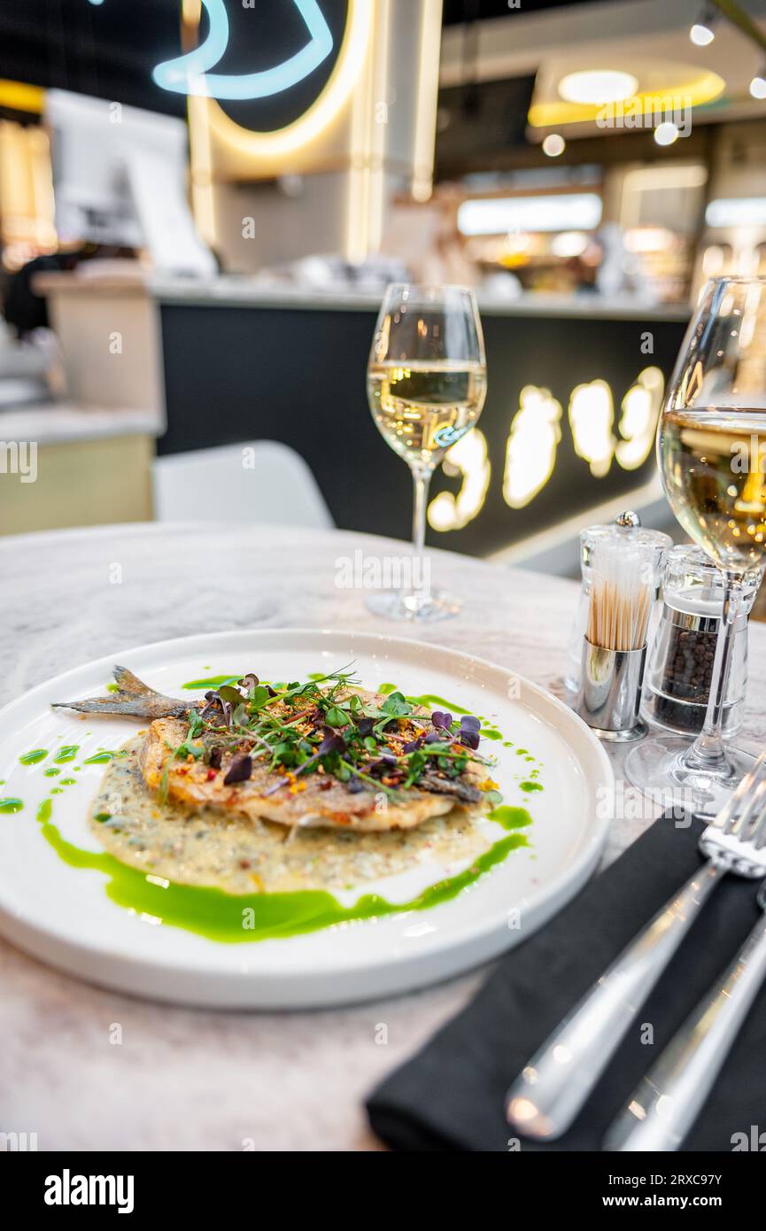 Sea bass in cream sauce with Provencal herbs and green olive oil on a white plate on a marble table in a restaurant Stock Photo