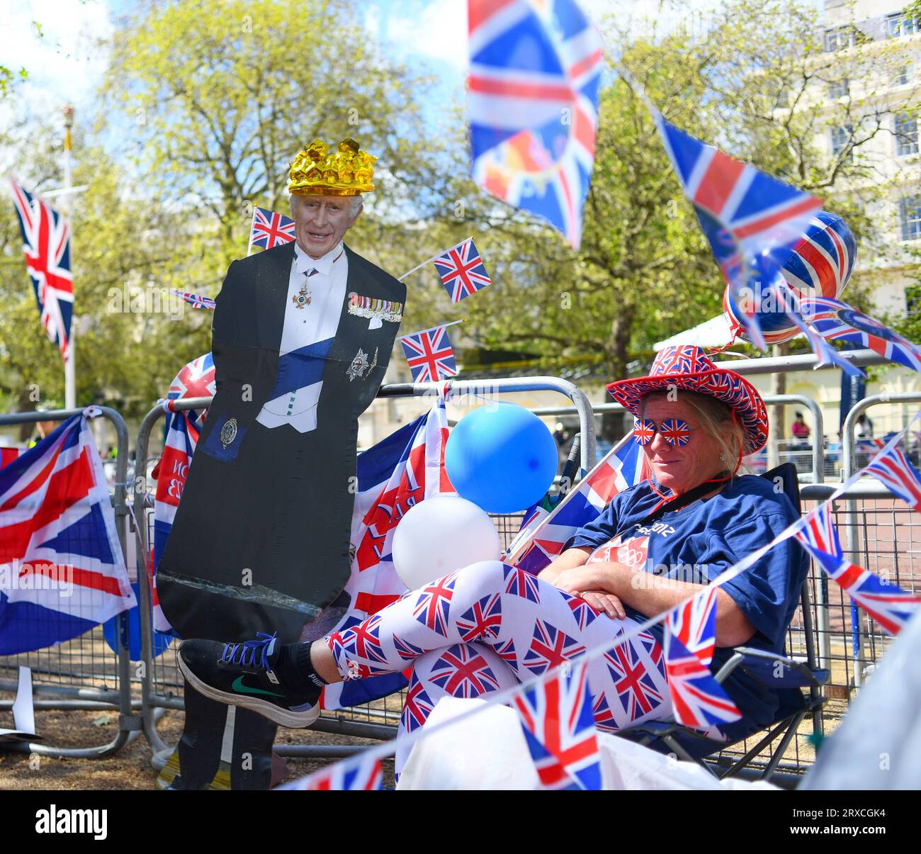 A lady sits next to a cardboard cut out of King Charles surrounded by Union Jack flags having secured her place on the Mall in London before the event Stock Photo