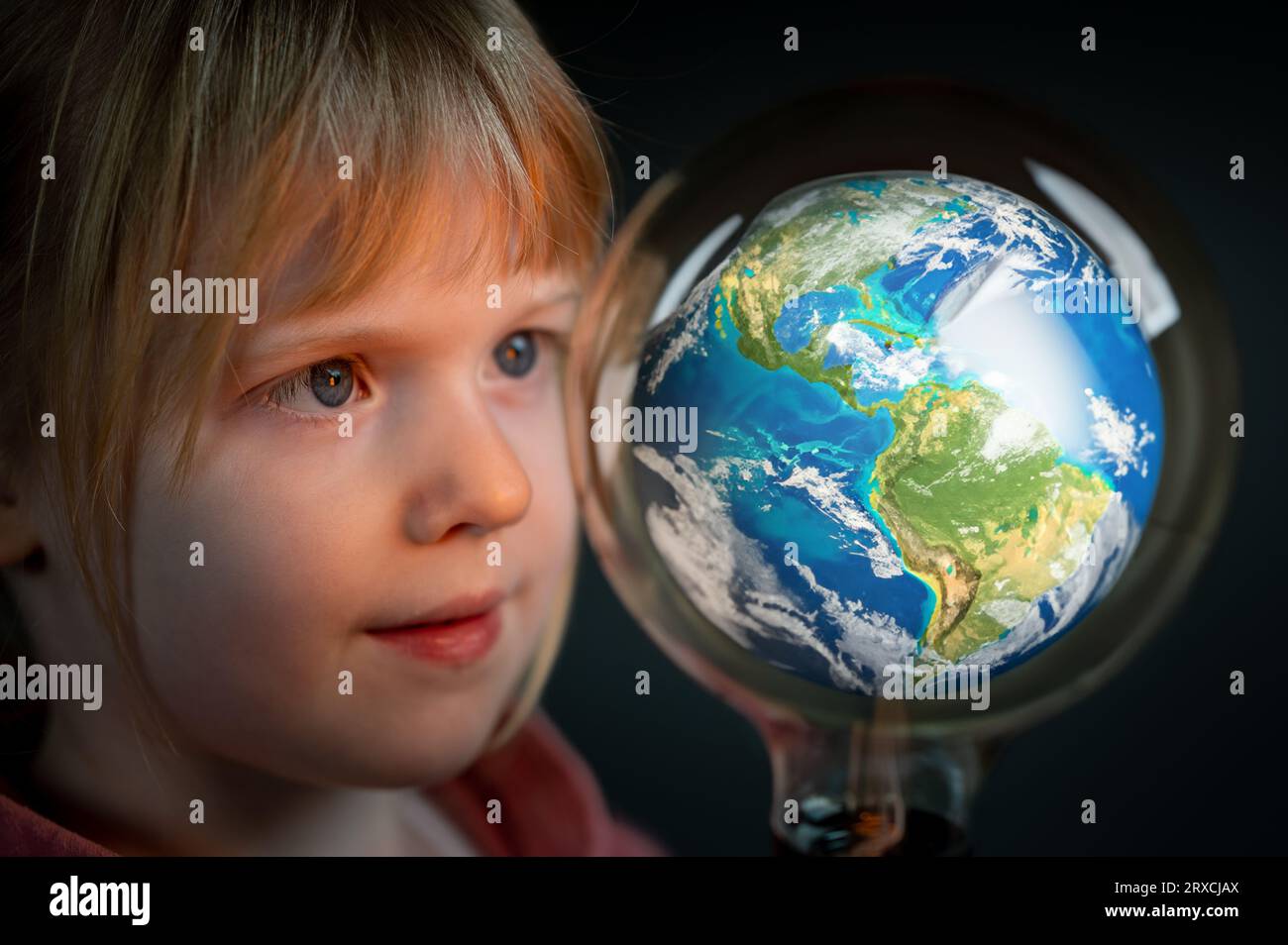 Young child looks focused to a model of the earth. Symbol for a curios