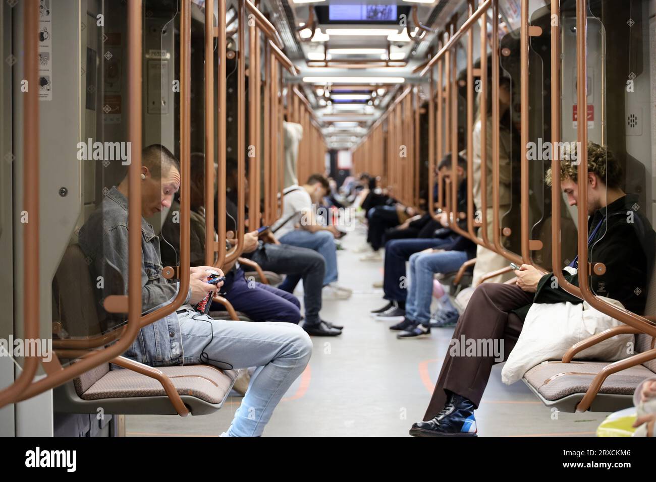 People in a metro train, guys sit with smartphone in the foreground. Interior of modern subway car Stock Photo