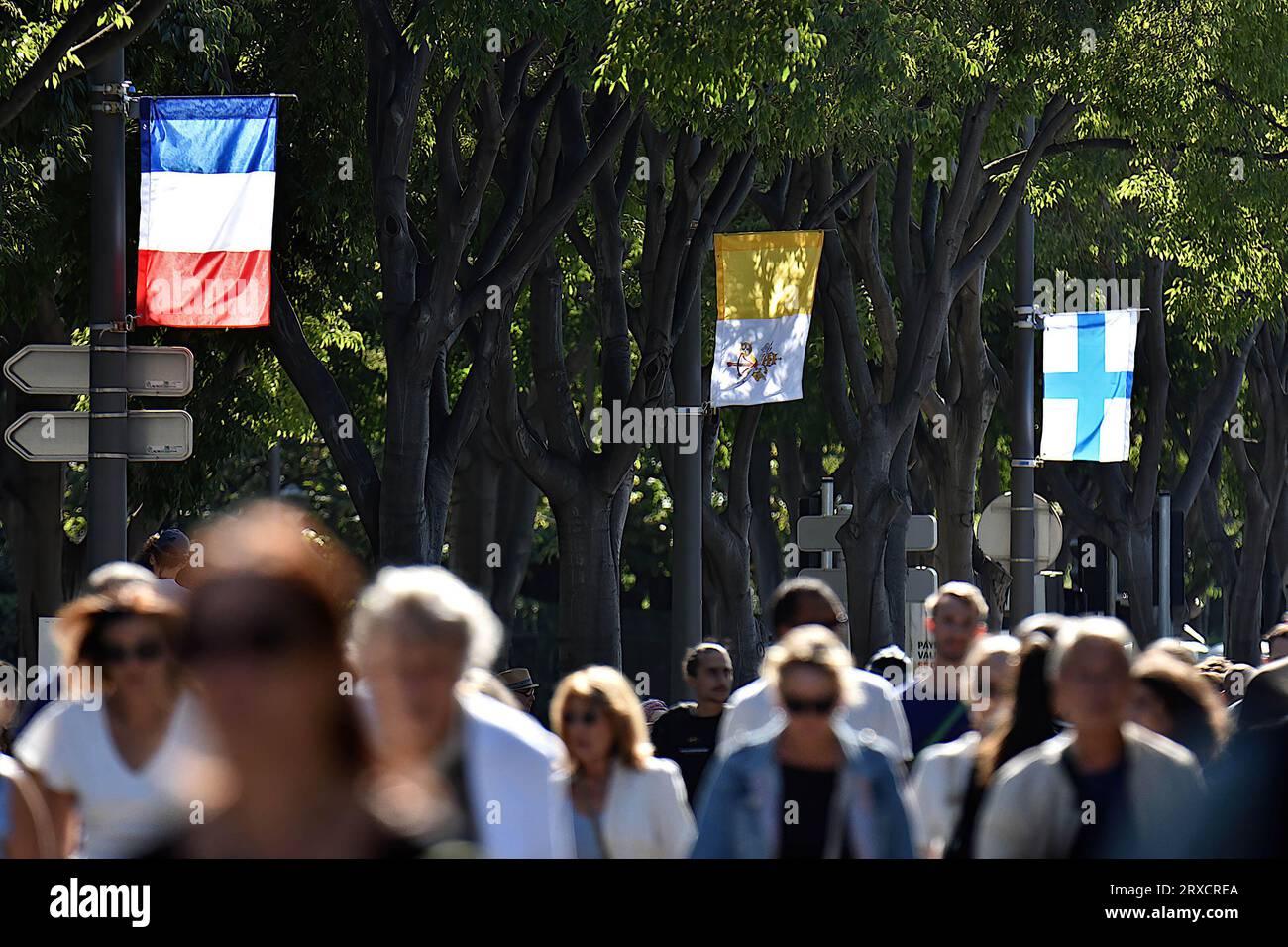 French, Vatican, and Marseille flags hang from street lamps. Thousands of people came to see Pope Francis stroll in his “Papamobile” on Avenue du Prado, they attended the high mass on giant screens at the Vélodrome stadium. Stock Photo