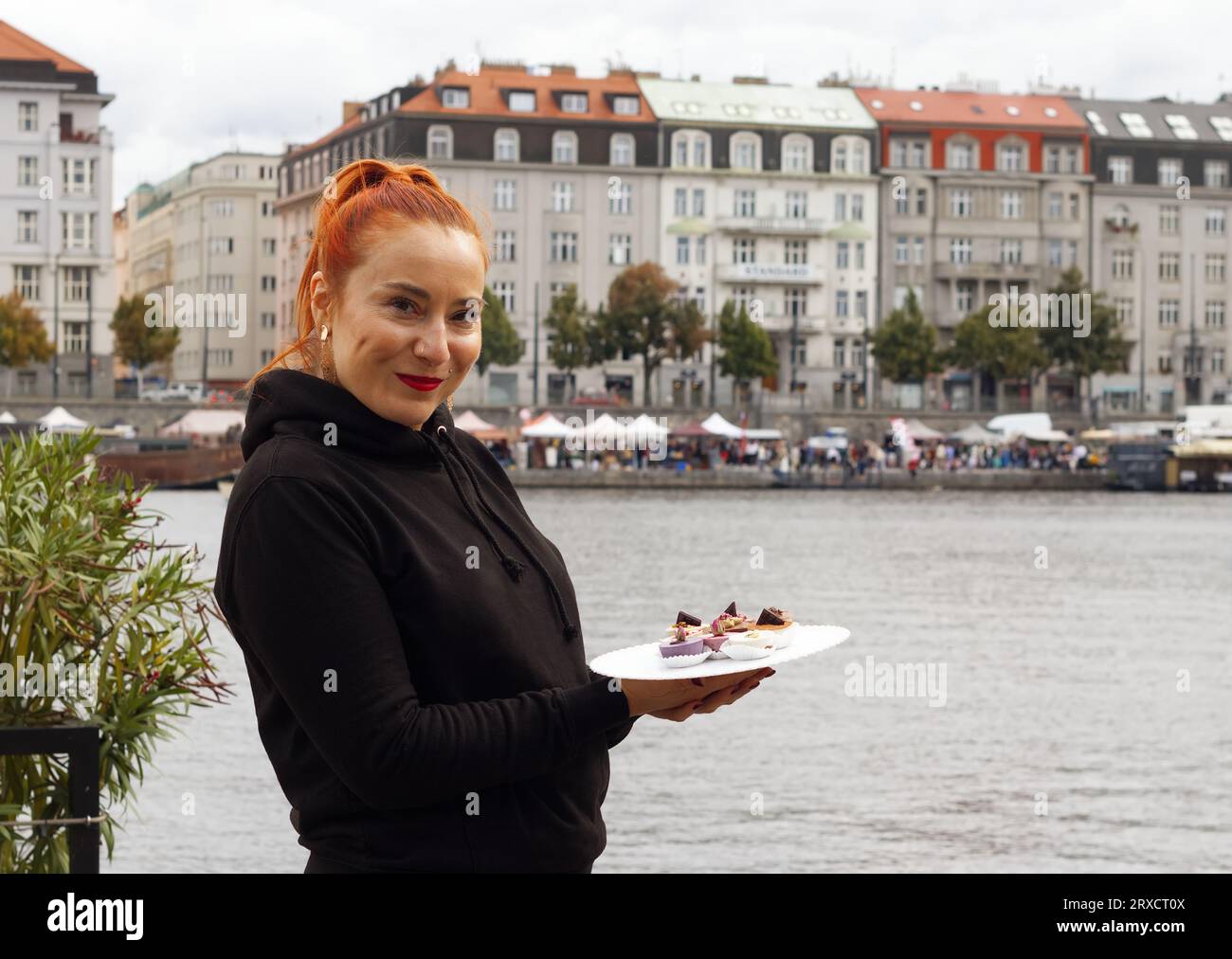 Pretty young vendor poses with an array of mini cheesecakes at the food festival on the Smichov waterfront. Stock Photo