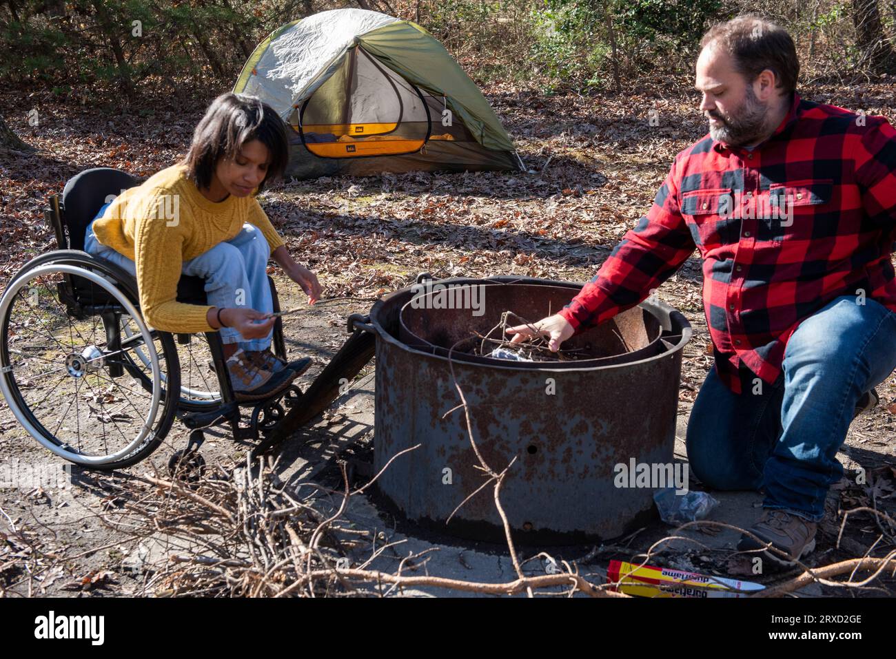 An outdoorsy couple starts a campfire at their campsite. Both are disabled but love the outdoors. Stock Photo
