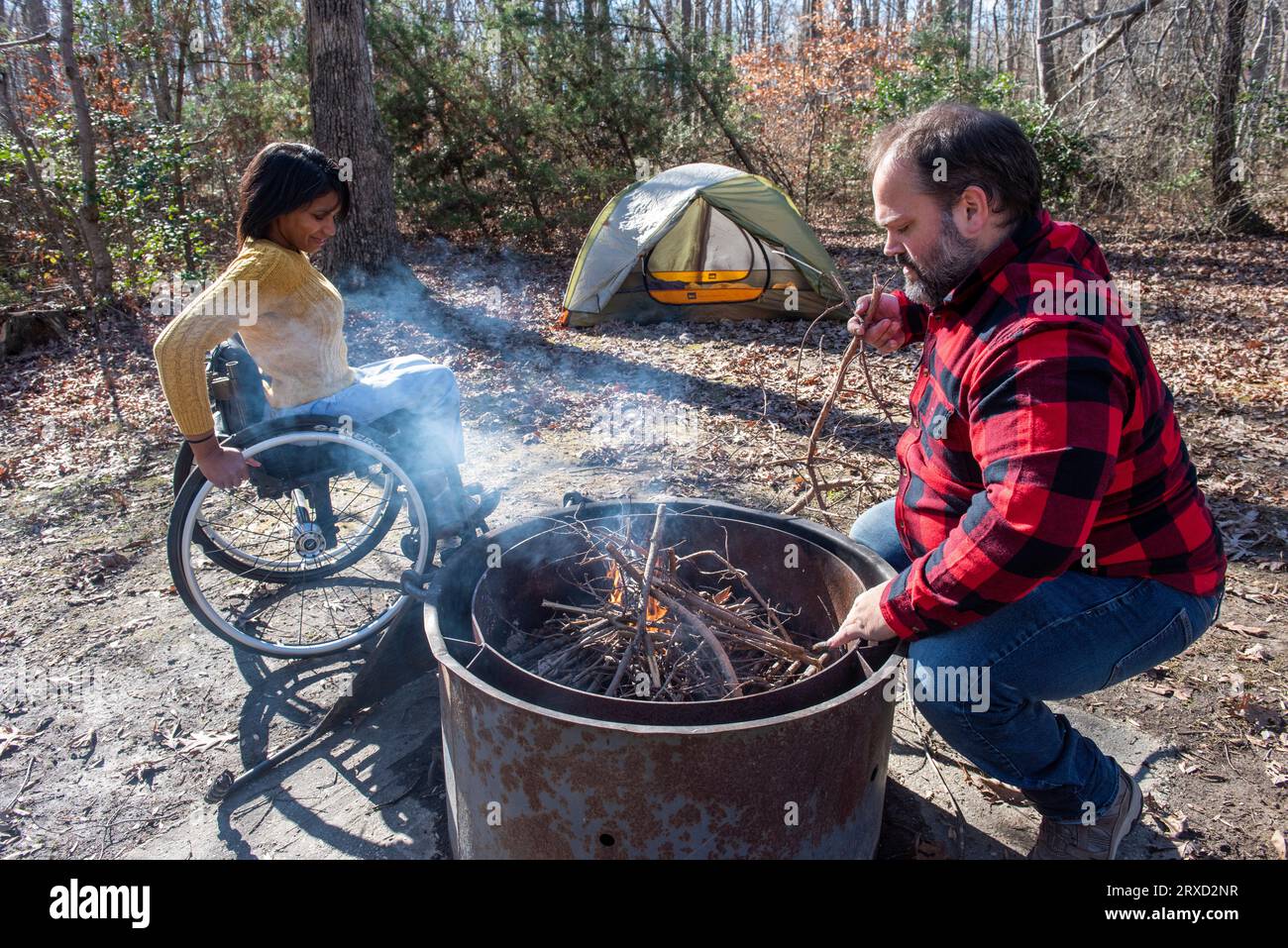 An outdoorsy couple starts a campfire at their campsite. Both are disabled but love the outdoors. Stock Photo