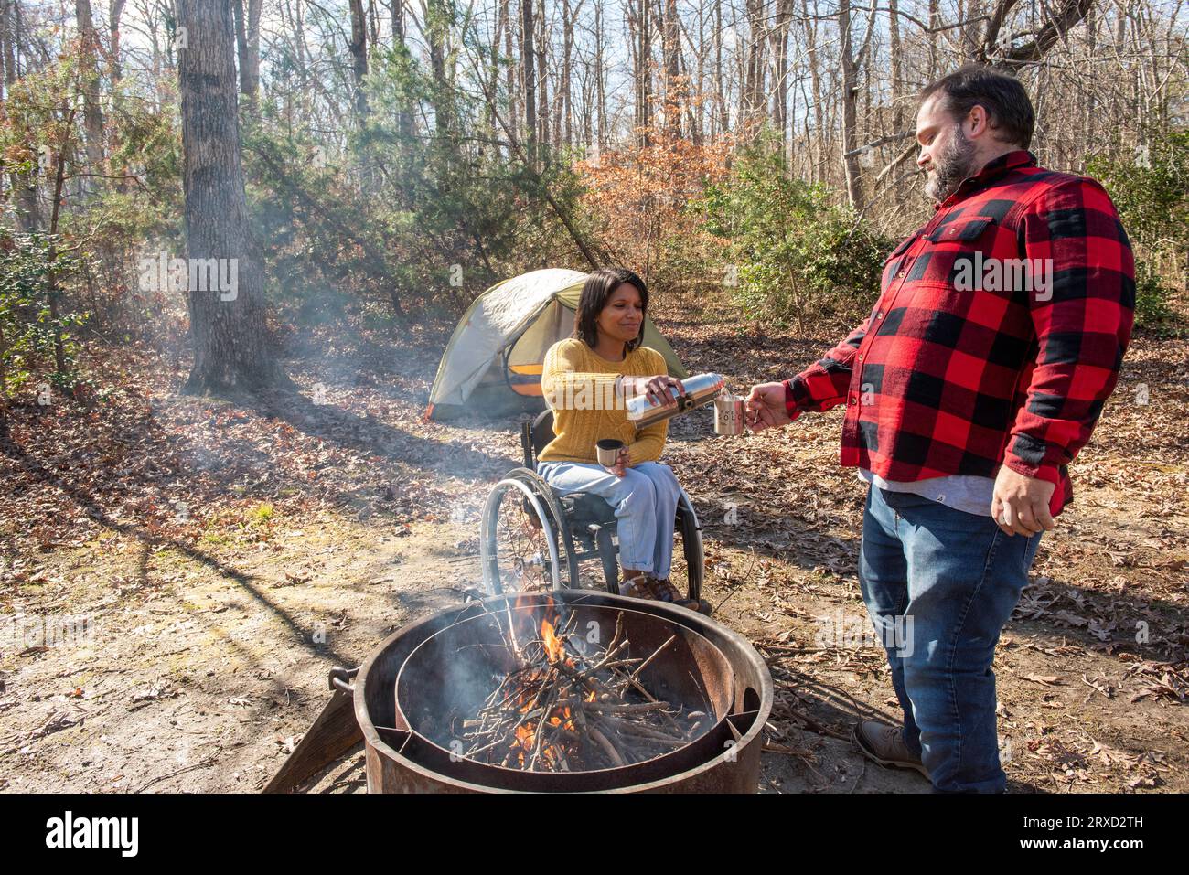 An outdoorsy couple shares a hot beverage to stay warm at their campsite. Both are disabled but love the outdoors. Stock Photo
