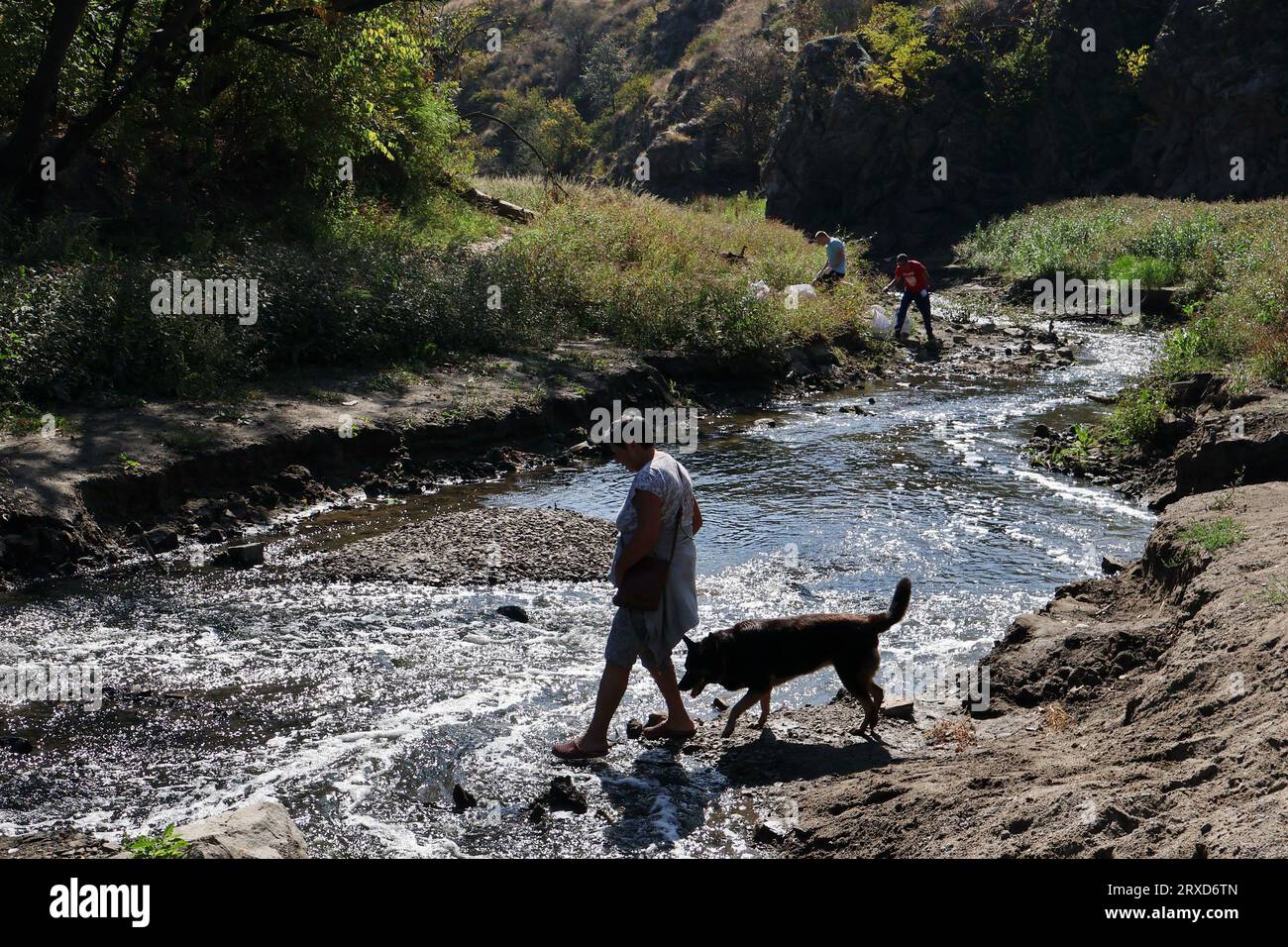 Zaporizhzhia, Ukraine. 18th Sep, 2023. A woman with her dog seen crossing the river while volunteers clean a river from the garbage as water in Dnipro river dropped more than 4 meters after the explosion of the Kakhovka dam in Zaporizhzhia. The commander of the Tavria group troops, Oleksandr Tarnavskyi (Ukraine), said that the Defence Forces had broken through the Russian defences in Verbove, Zaporizhzhia region. He adds that the main thing is not to lose the initiative that the Ukrainian army has now. (Credit Image: © Andriy Andriyenko/SOPA Images via ZUMA Press Wire) EDITORIAL USAGE ONLY Stock Photo