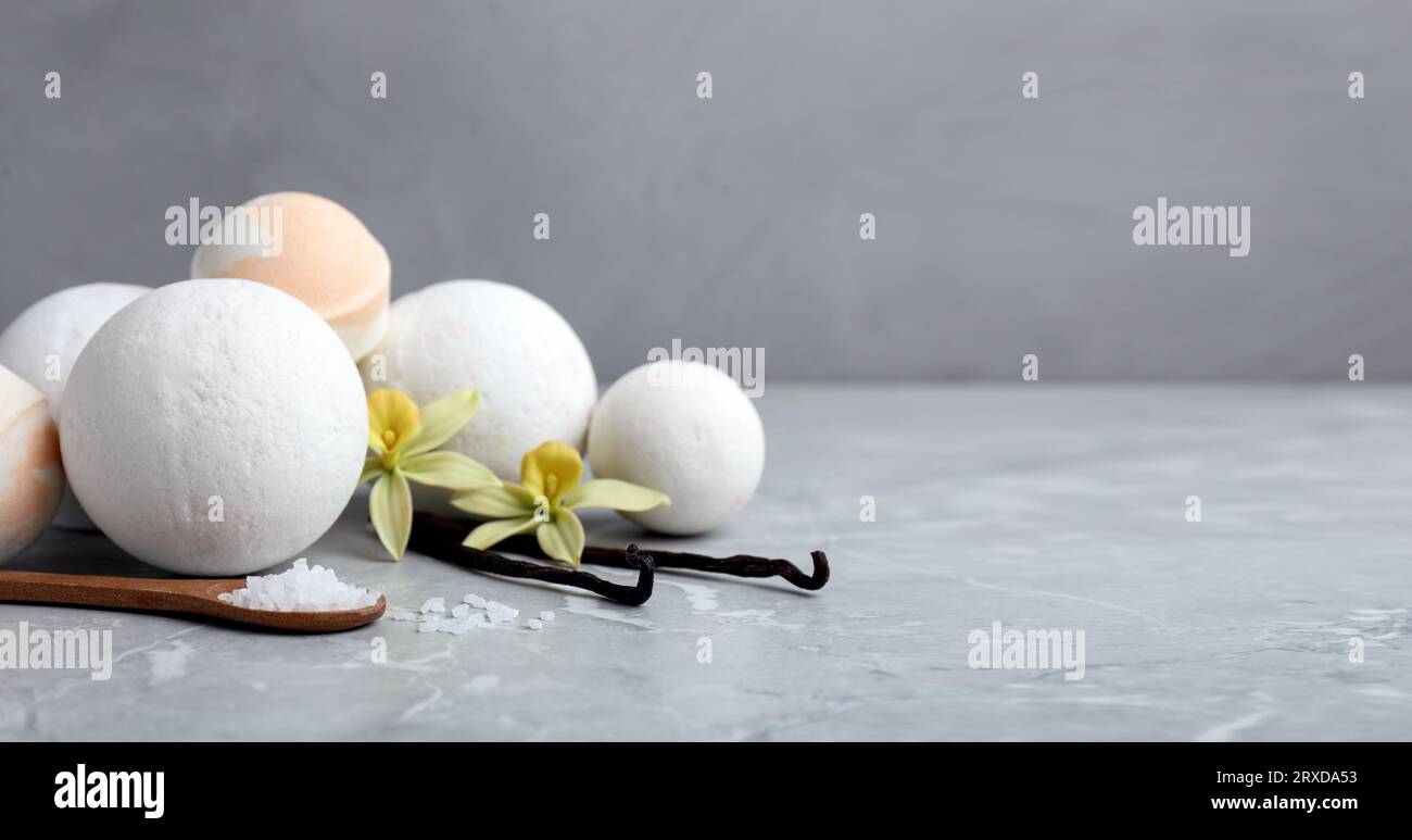 Many different bath bombs with vanilla sticks and flowers on light grey table. Space for text Stock Photo