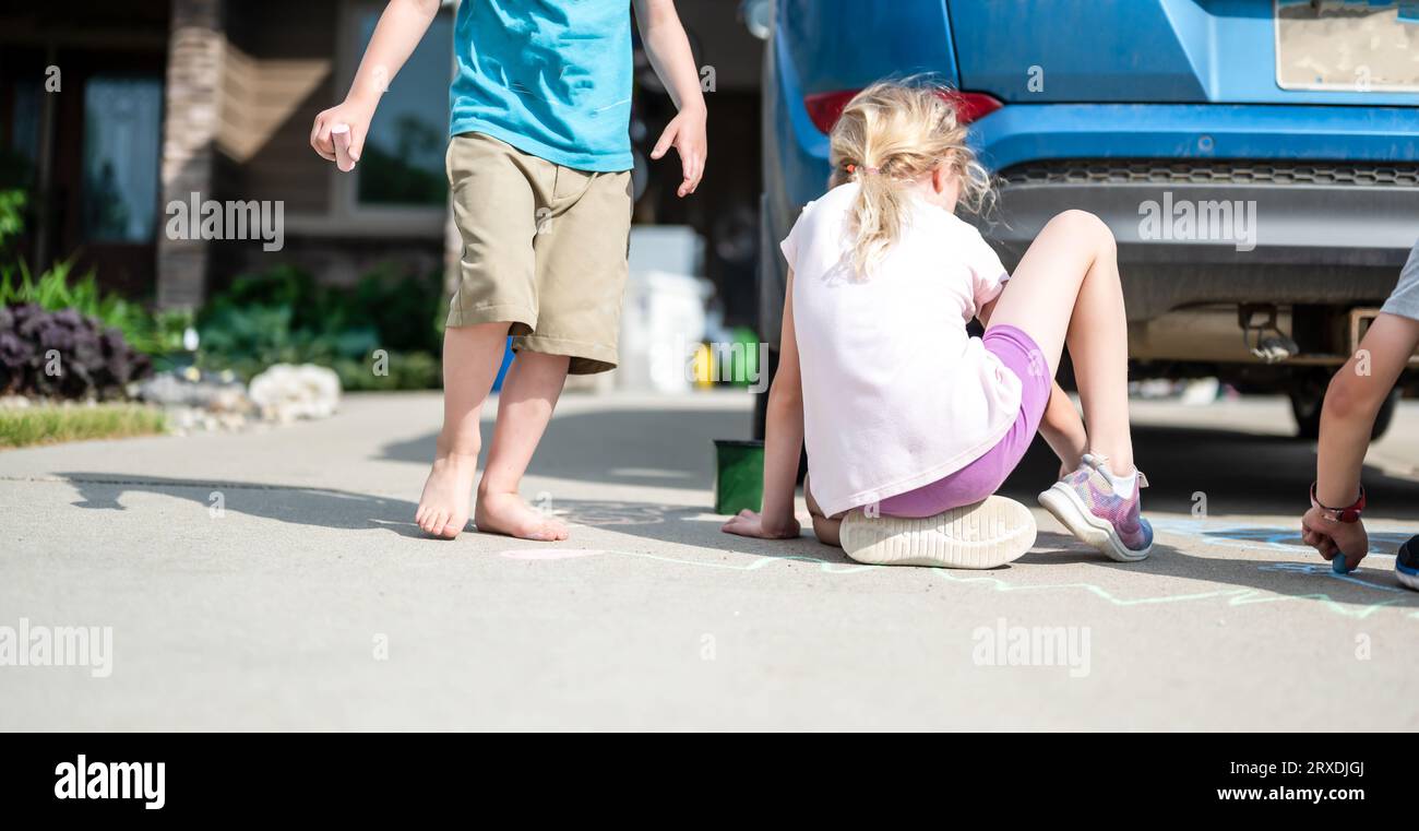 Children sitting on a driveway behind a vehicle in a blind spot out of view of the driver.  Stock Photo