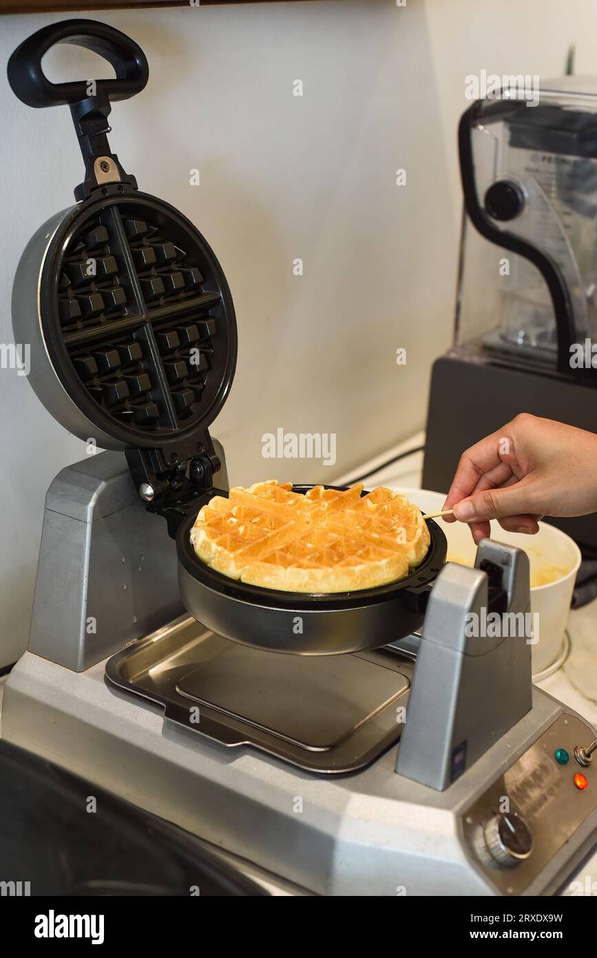the cook check the dough for sweet waffles into the waffle iron with a wooden stick Stock Photo