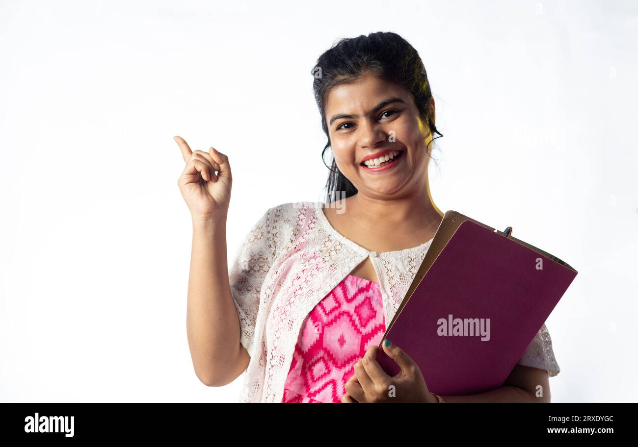 A pretty young Indian girl with books in hand pointing with smiling ...