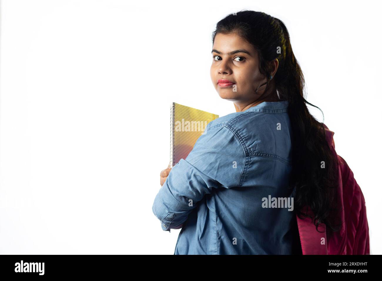 A pretty young Indian girl with books in hand and backpack looking back ...