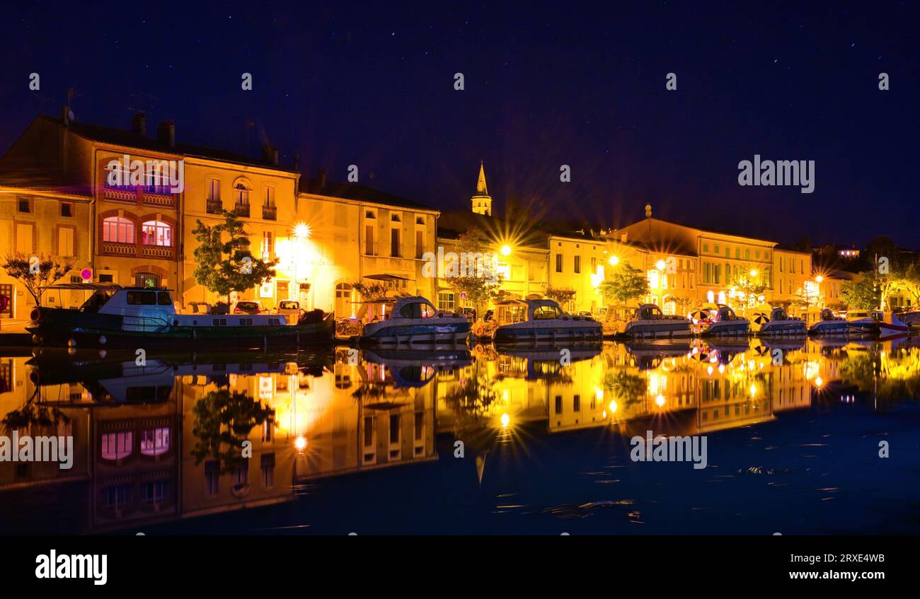 Castelnaudary Aude France 09.24.23 Town Harbour at night on the Canal du Midi. Row of river cruisers moored beside a row of illuminated buildings. Stock Photo