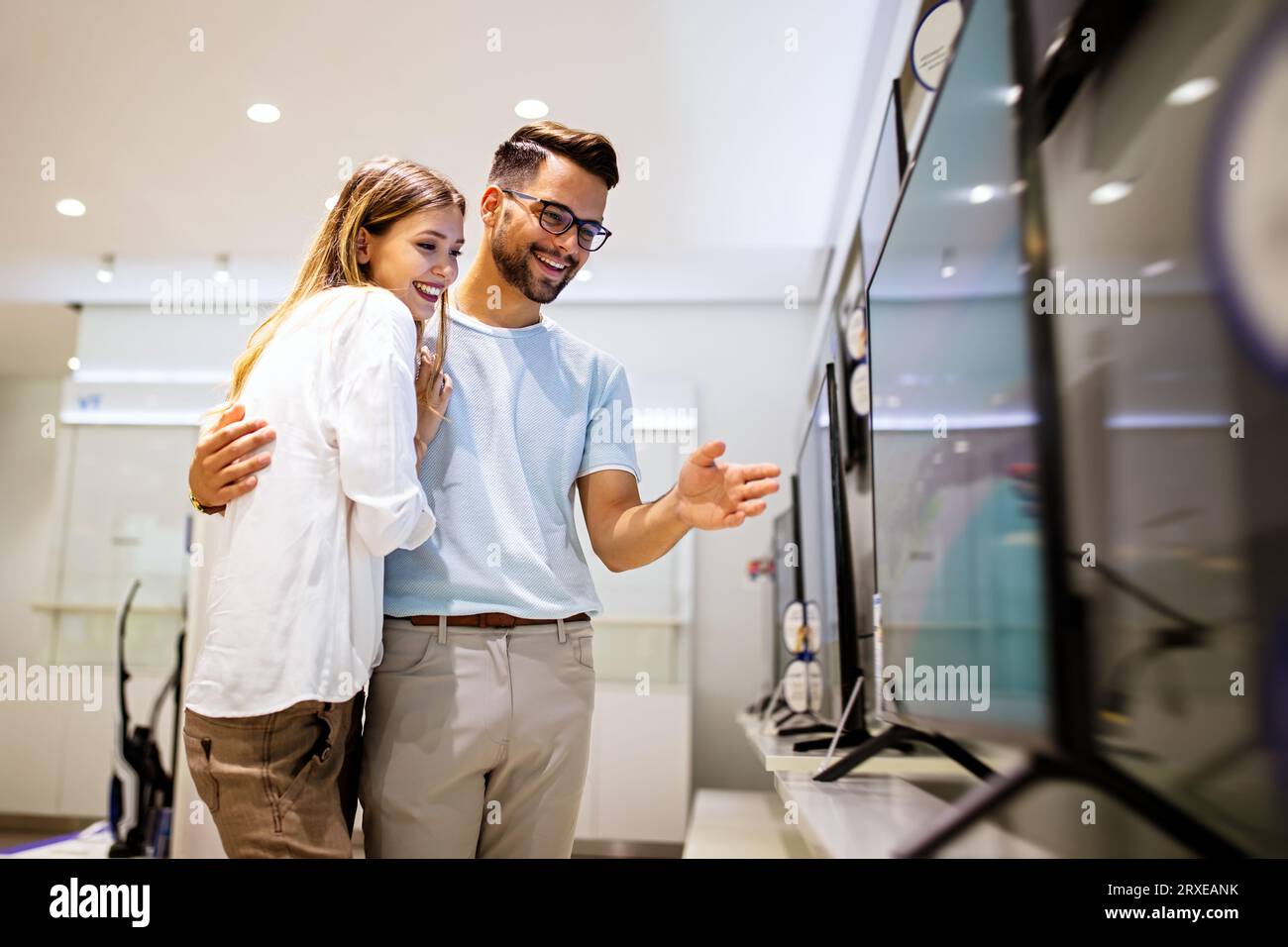 Young couple in consumer electronics store looking at latest digital devices, television. Stock Photo