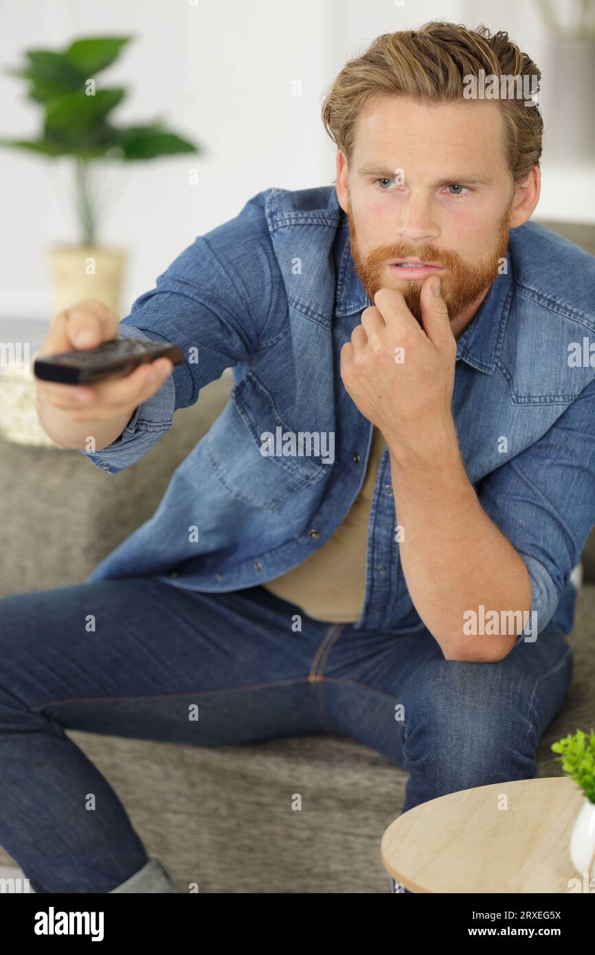 young man changes the channels on the remote control Stock Photo