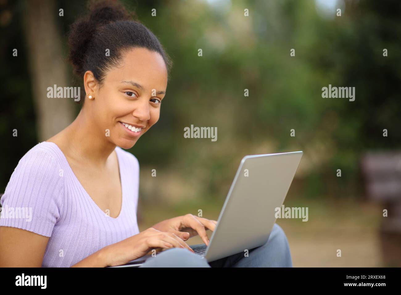 Black woman looks at you using laptop sitting in a park Stock Photo