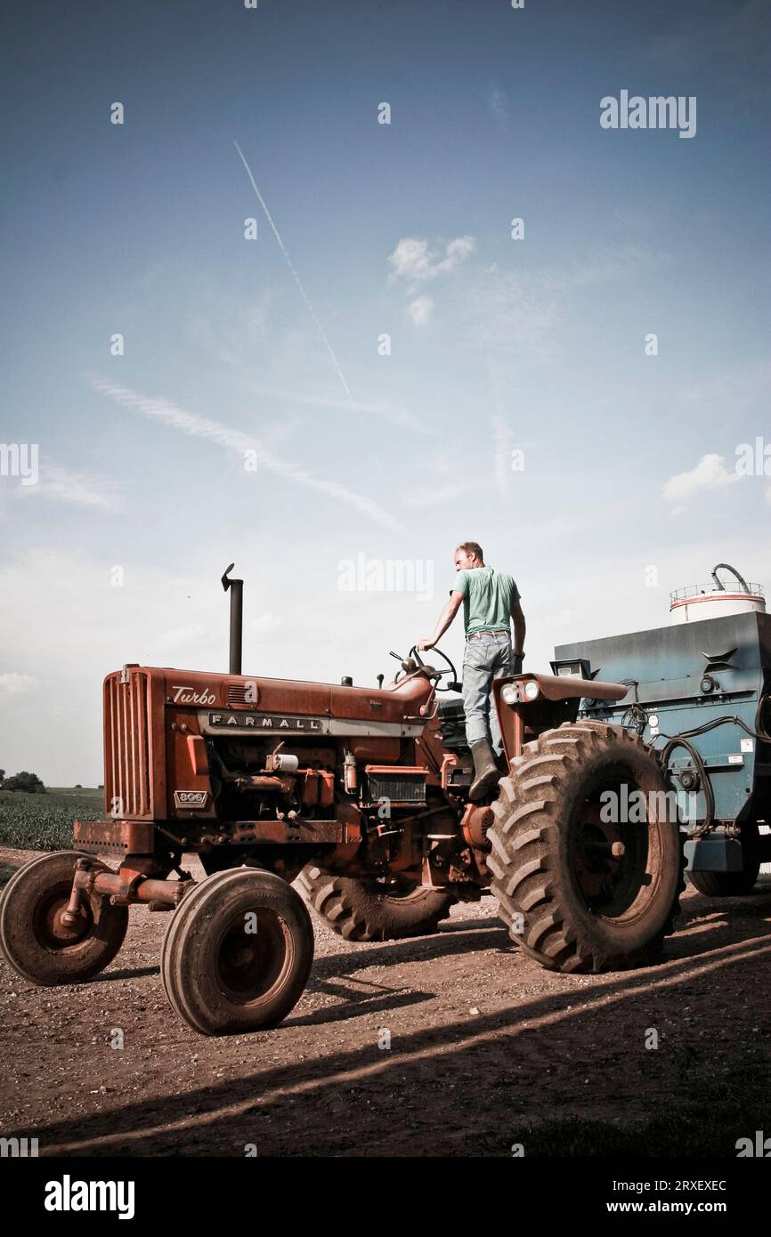 A man stands on the tractor to get a better view of the field on their family farm in Keymar, Maryland. Stock Photo