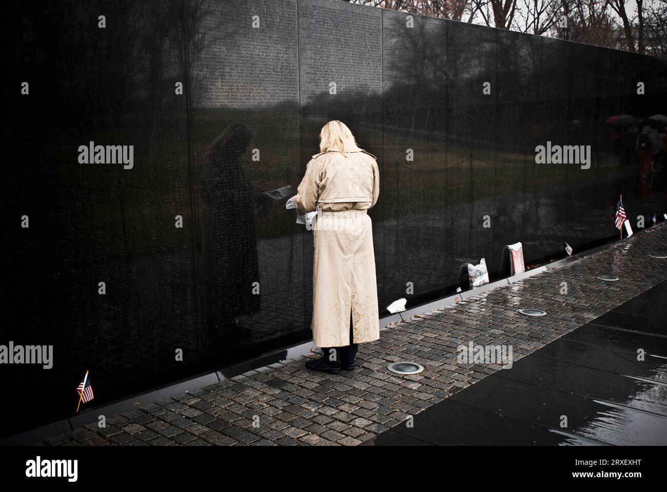 A woman in a rain coat facing the engraved wall of the Vietnam War