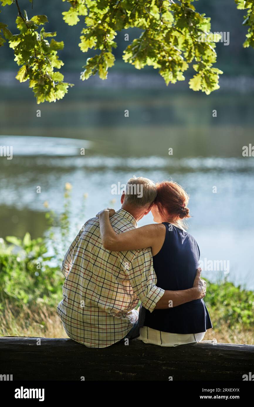 back senior man and woman sitting hugging by the water Stock Photo