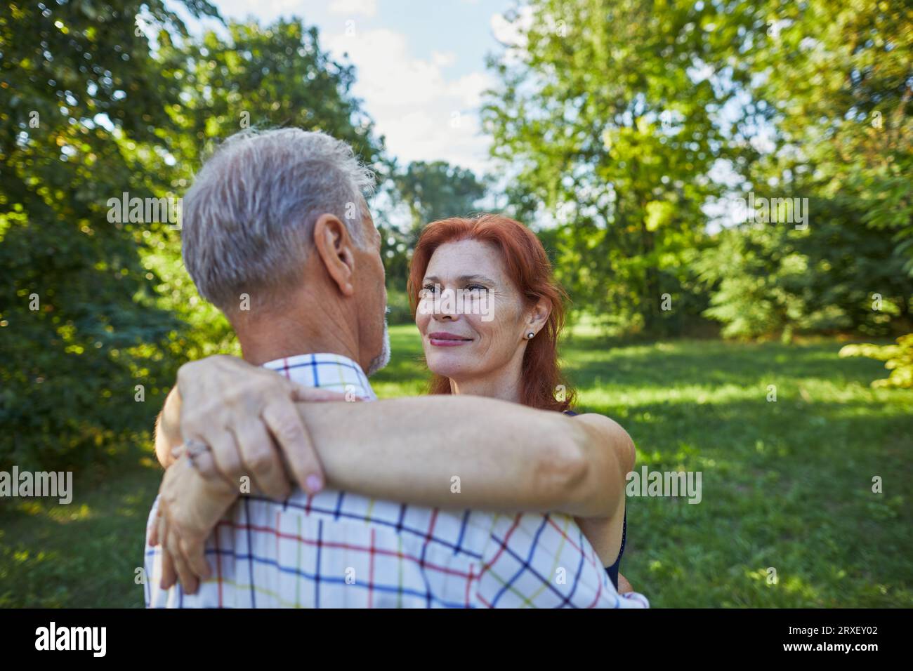 smiling senior woman with red hair hugs a man and looks at him Stock Photo