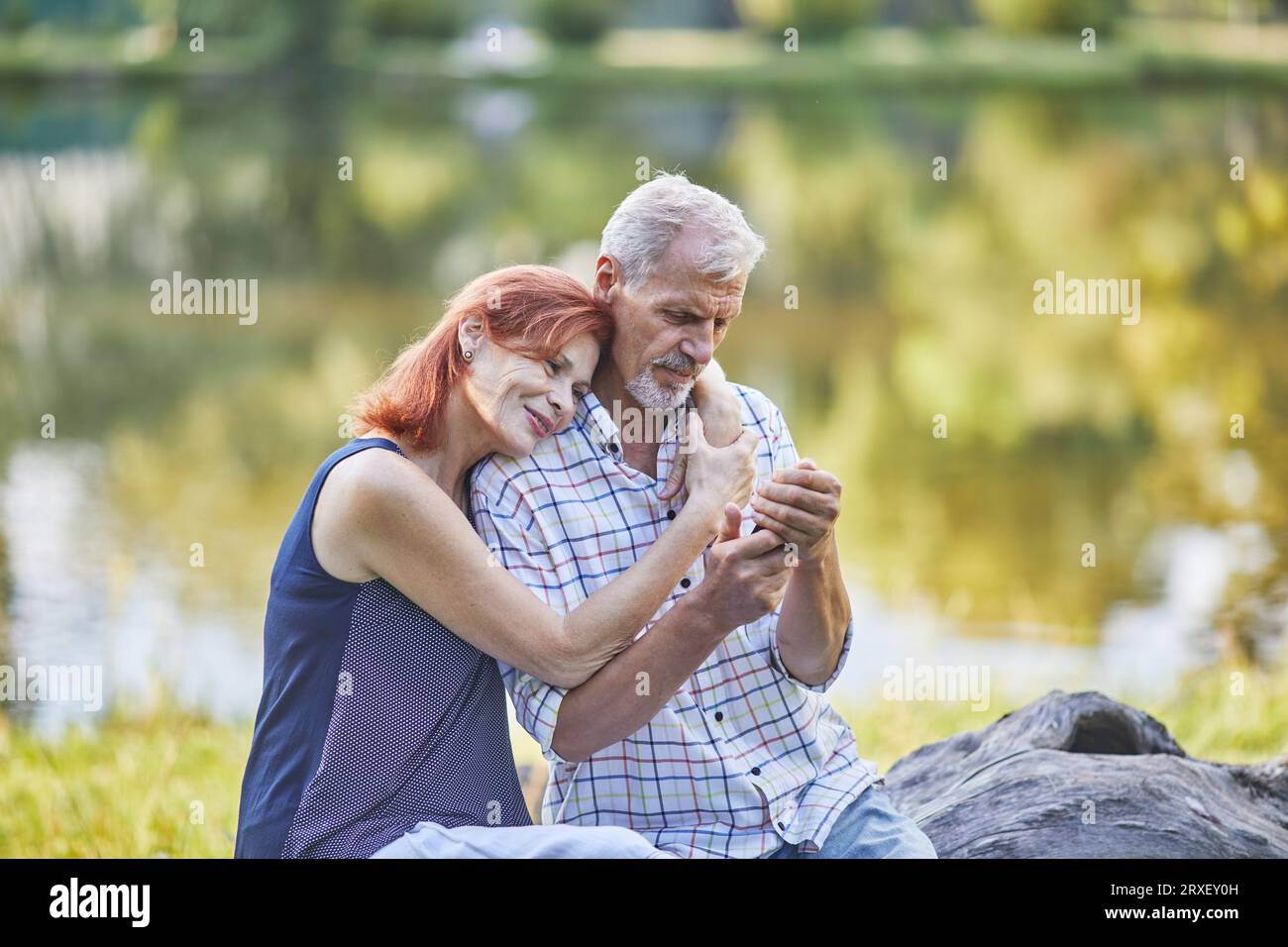 senior  woman hugging a man who is looking at the phone on outdoor Stock Photo