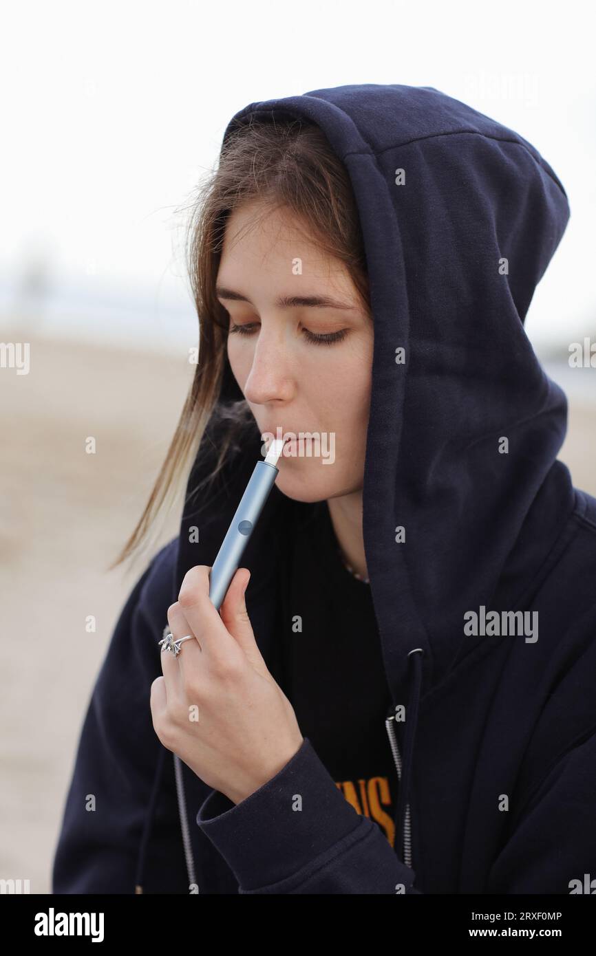 Electronic cigarette technology. Young woman smokes and releases steam from  hybrid cigarette device that uses real tobacco refills with a heating pad,  tobacco heating system. Bad unhealthy habit Stock Photo