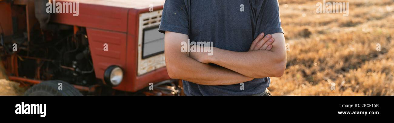 A farmer stands in front of a agricultural tractor. Stock Photo