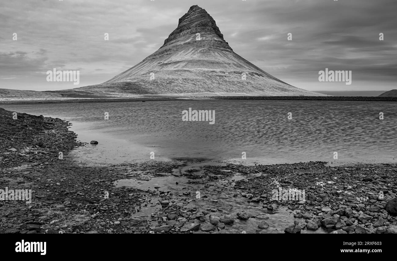 Kirkjufell's shadowed reflection, a monochrome memory where land, water, and clouds entwine. Stock Photo
