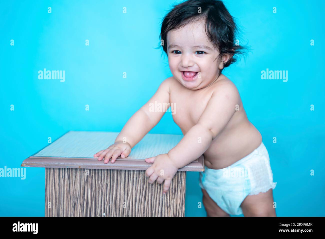 Smiling six months old cute indian baby boy wearing diaper trying to