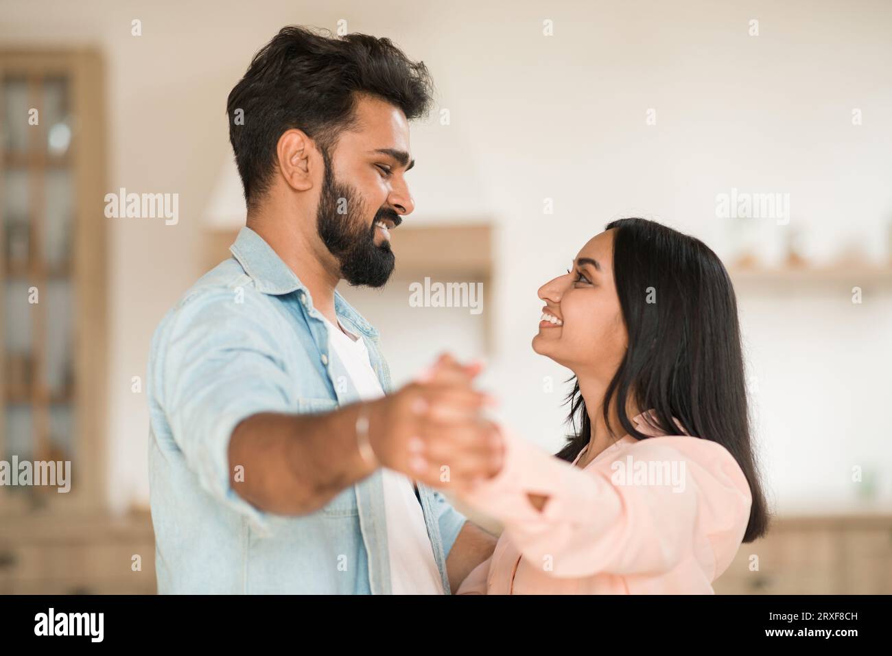 Romantic indian couple enjoying time together at home, dancing waltz, holding hands and smiling to each other Stock Photo
