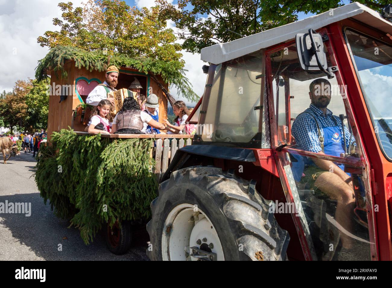 a tractor pulls the cart, a family dressed in costumes plays music in the Almabtrieb parade Stock Photo