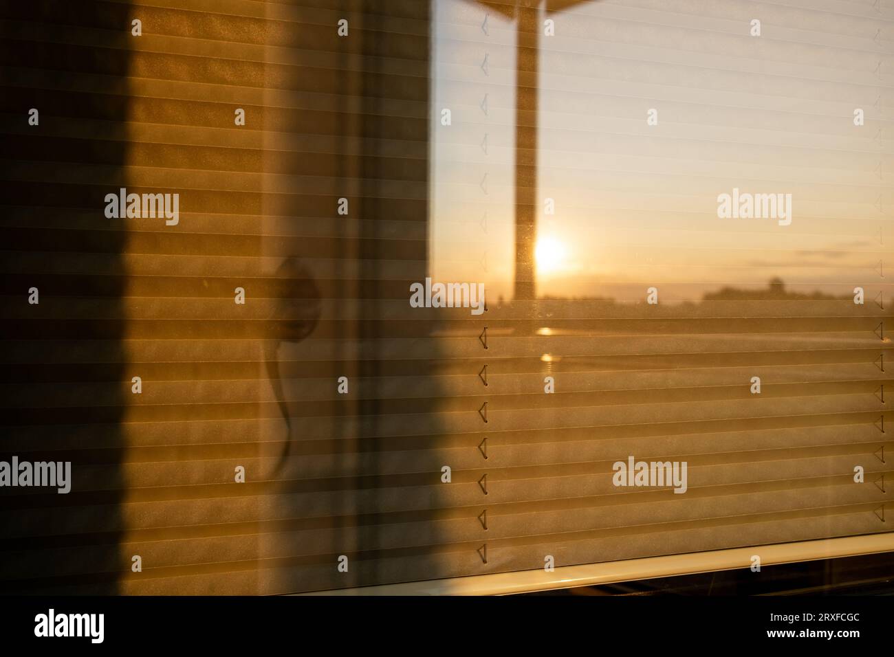 View of the window from the outside, closed with blinds, the setting sun is visible in the reflection Stock Photo
