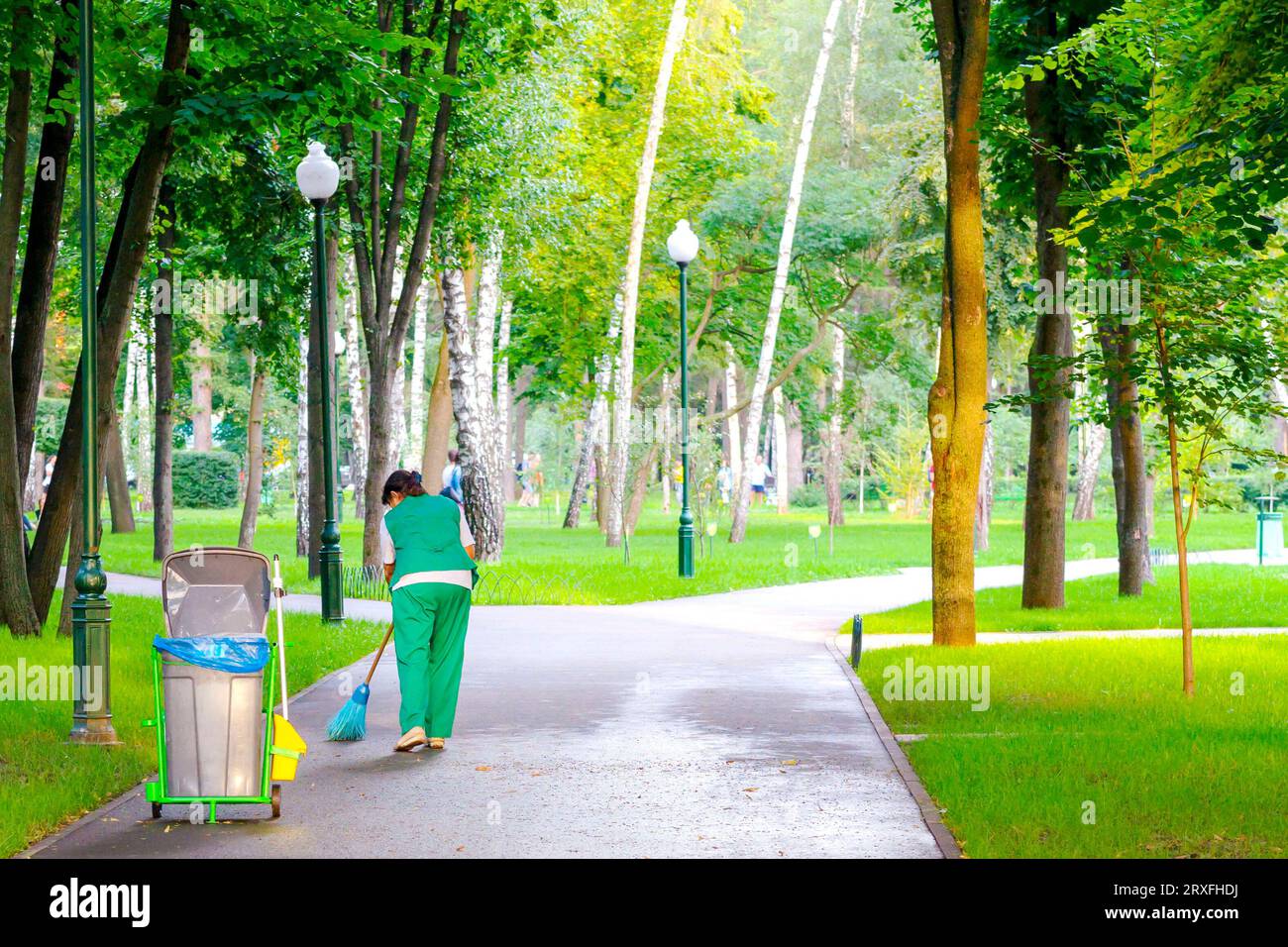 The janitor is working. The woman the cleaner collects garbage in the park alley. sanitation worker sweep street Stock Photo