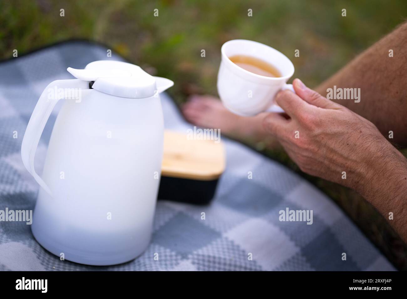 ILLUSTRATION - 17 September 2023, Berlin: A thermos flask stands on a picnic blanket, while in the background a man holds a cup of warm tea in his hand. (to dpa: 'The thermos flask and the somewhat hapless history of its inventor ') Photo: Monika Skolimowska/dpa Stock Photo