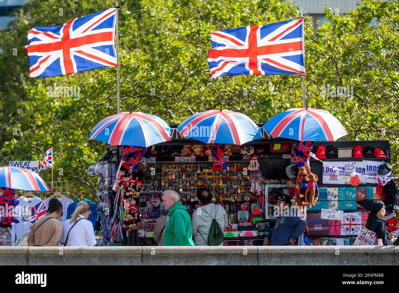 London, UK.  25 September 2023.  UK Weather : Tourists in front of Union Jack flags fluttering in the breeze atop a souvenir stand on Westminster Bridge in the sunshine and temperatures of 22C.  The autumnal equinox occurred two days ago meaning that days will be shorter and nights longer.  Credit: Stephen Chung / Alamy Live News Stock Photo